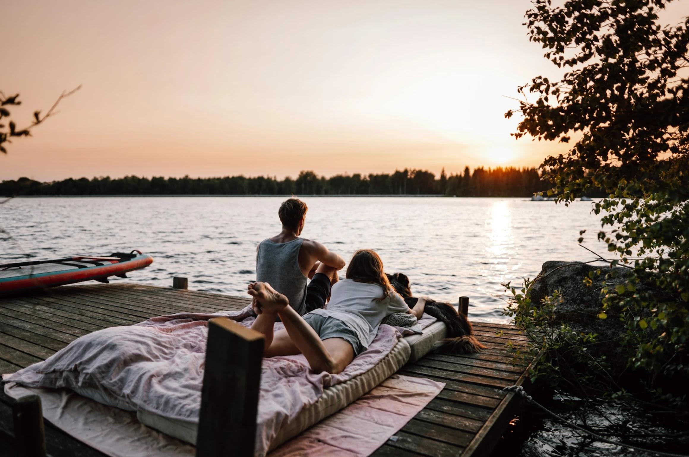 A couple sitting on a dock staring out into the sunset